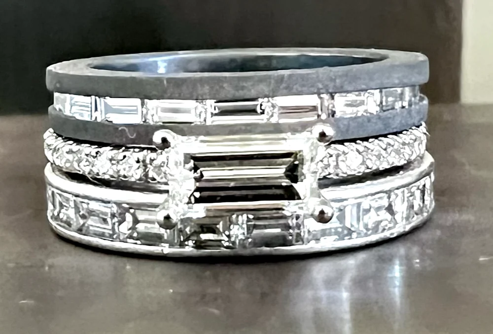 Vier Ringe übereinander: Baguette-Memoire in Weißgold, Verlobungsring mit quer
        gestelltem Baguette-Diamanten, darüber zwei Ringe aus Titan