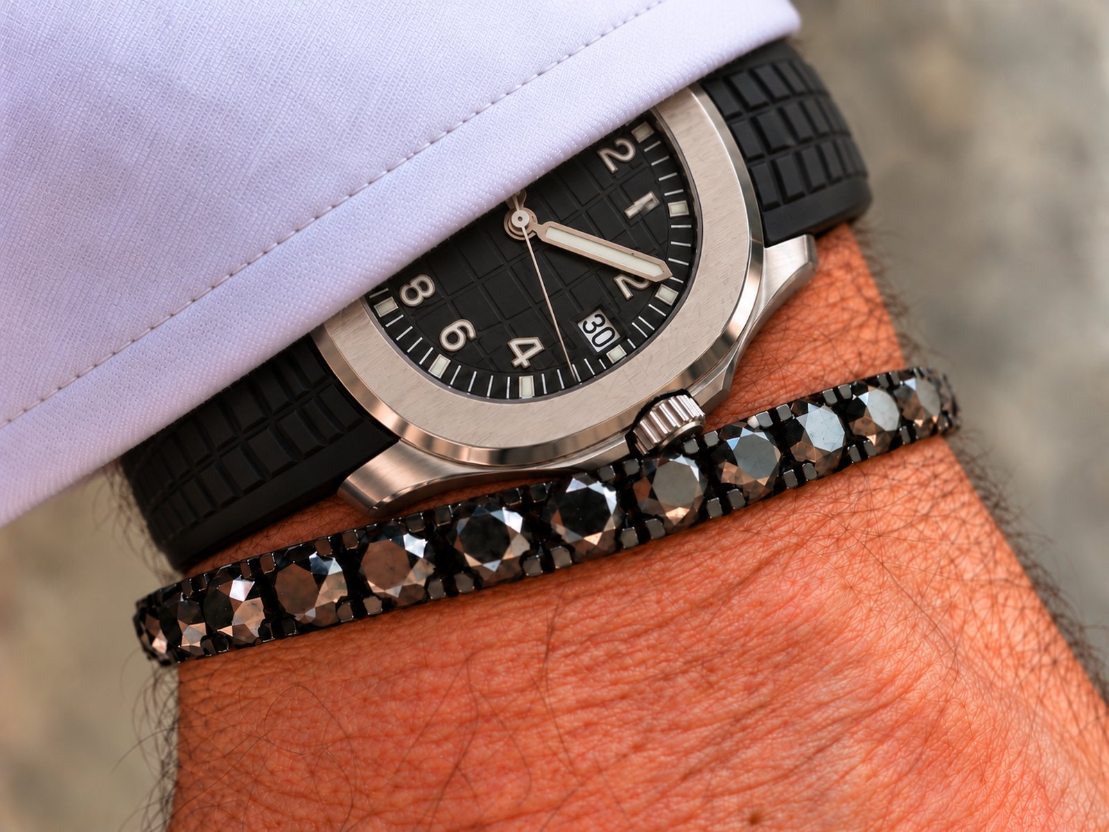 Schwarzes Stretch-Tennisarmband für Herren am Handgelenk neben einer Taucheruhr: schwarze Diamanten in DLC-beschichtetem Gold